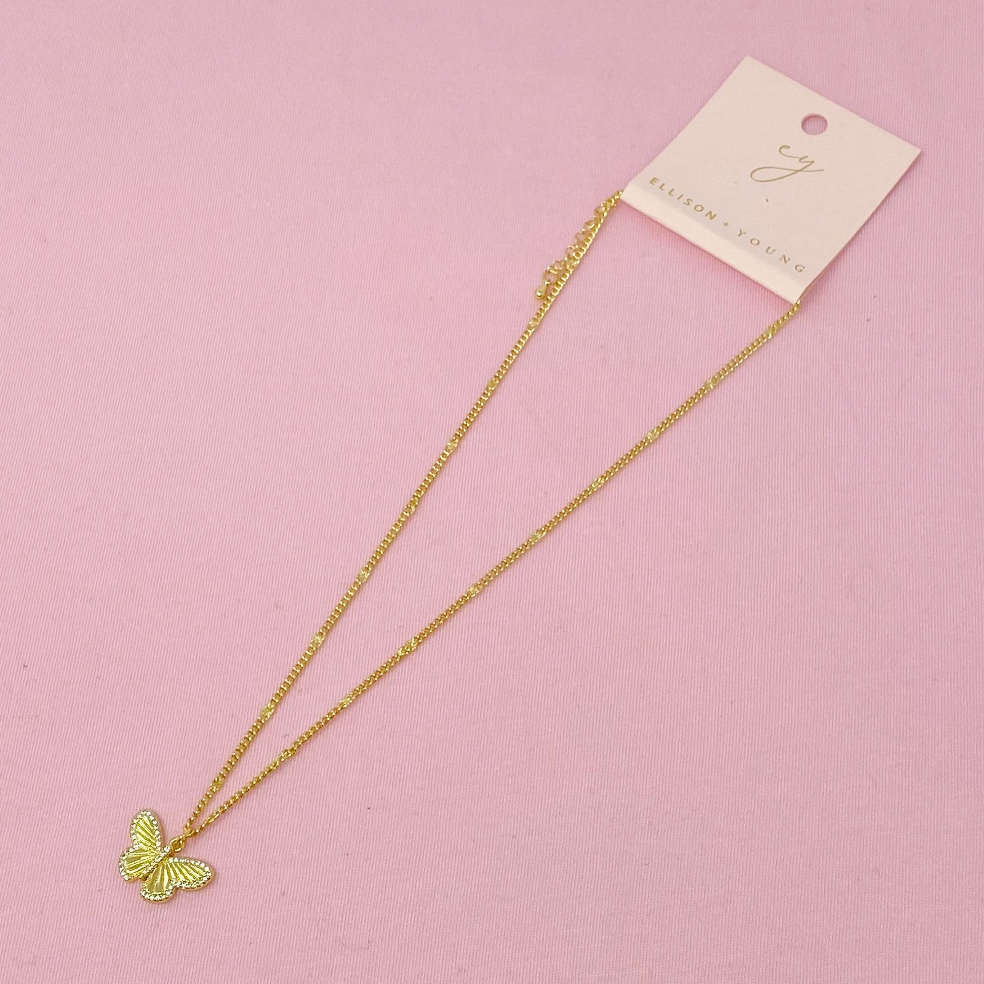 Gold butterfly pendant necklace on a delicate chain displayed on a pink background with a branded tag.