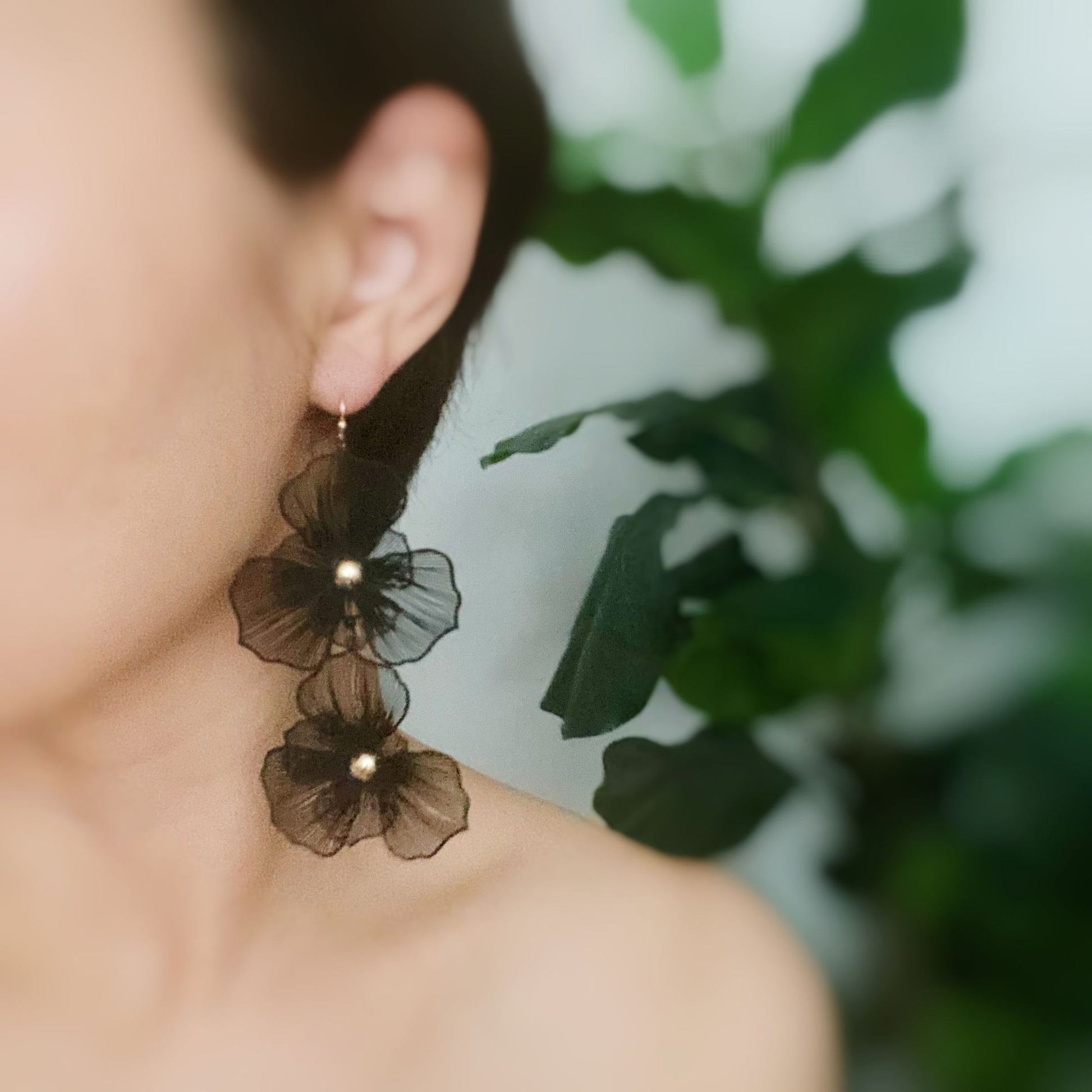 Elegant black floral earrings with pearl accents, worn by a woman with a simplistic background featuring green foliage.