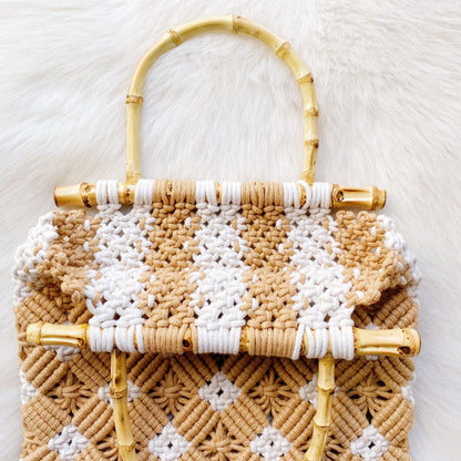 Handcrafted woven tote bag featuring a chic bamboo handle, with a stylish pattern in warm beige and white tones, set against a soft, textured background.