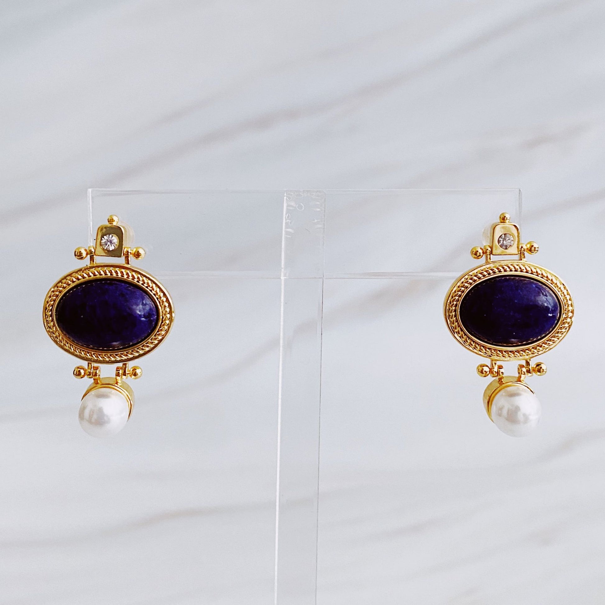 Elegant gold-tone earrings featuring deep blue lapis lazuli stones accompanied by a pearl drop, perfect for adding a touch of sophistication to any outfit.