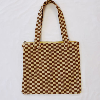Brown and cream checkered tote bag with handles, featuring a yellow zipper, displayed on white background.
