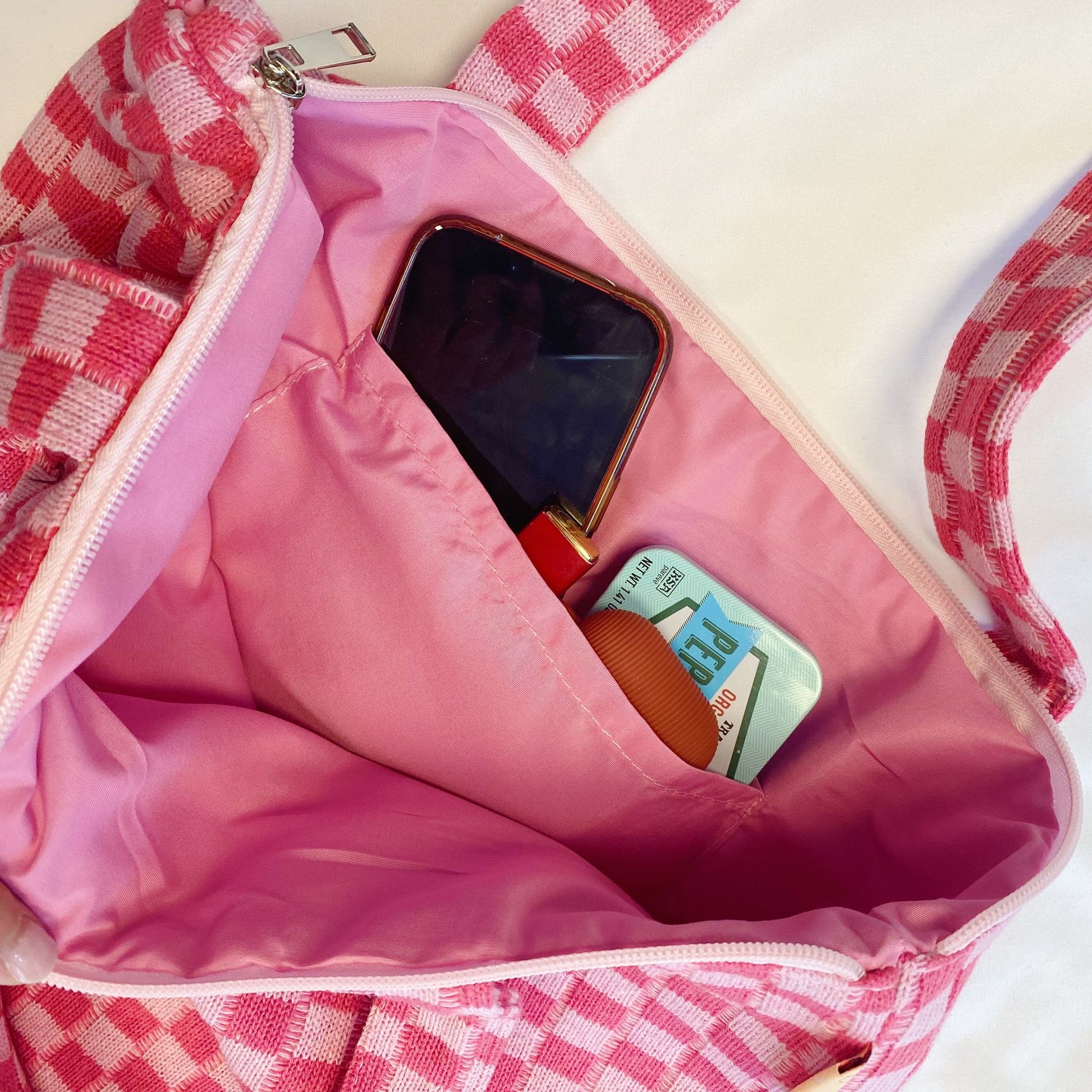 Colorful pink checkered bag interior showing essentials like a smartphone, lip balm, and hand sanitizer.