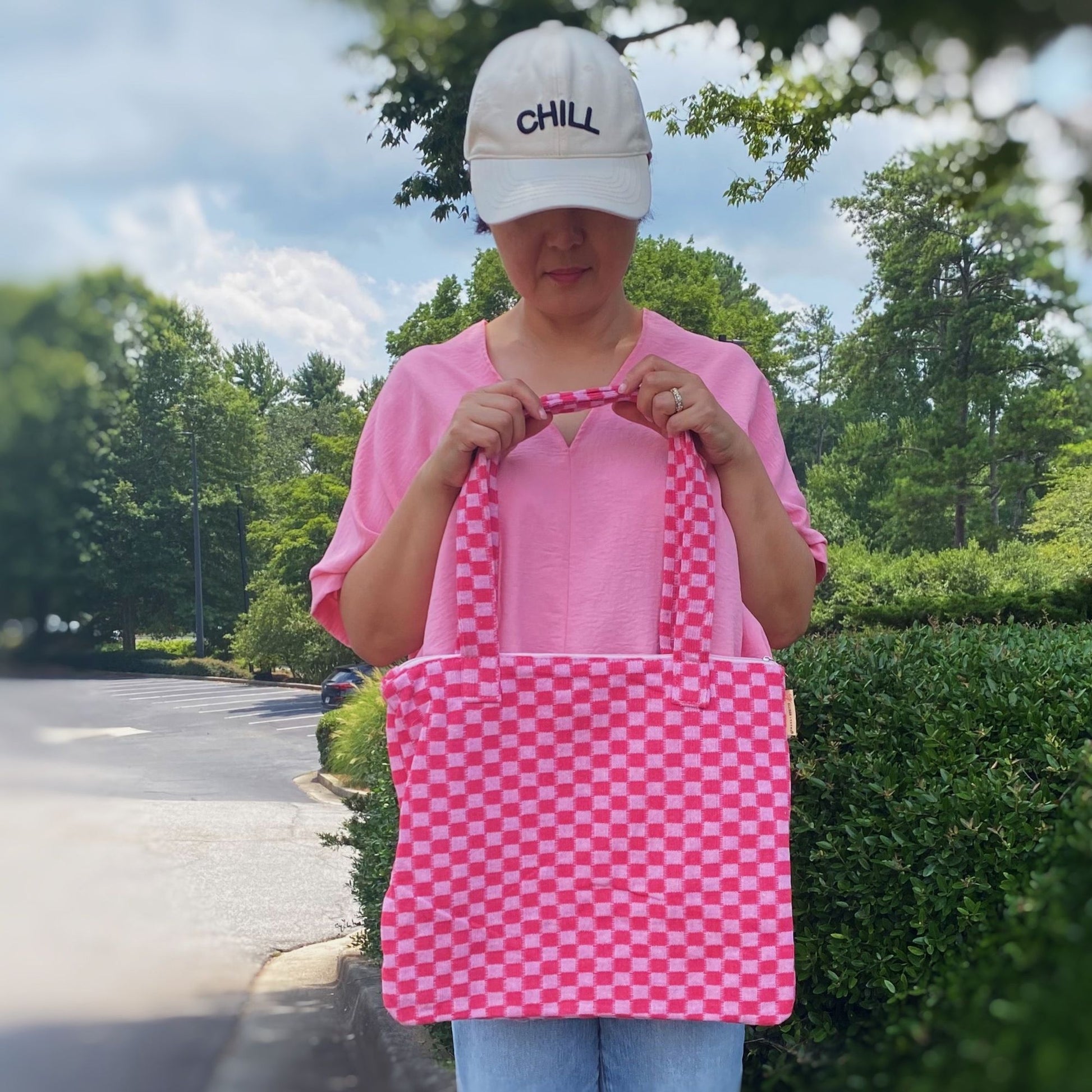 Colorful pink and white checkered tote bag with dual handles, showcasing a stylish and functional accessory for everyday use, set against a natural outdoor backdrop.