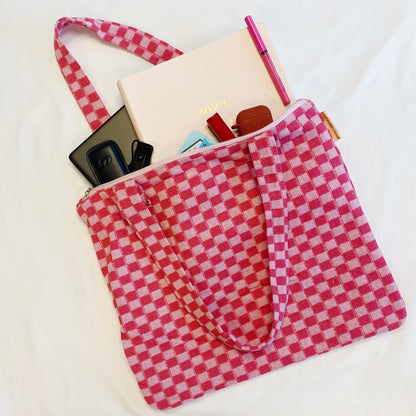 Pink gingham patterned tote bag filled with a planner, pens, keys, and cards against a white background.