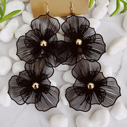 Black floral dangle earrings with golden accents displayed on smooth white stones, creating a stylish and elegant accessory.