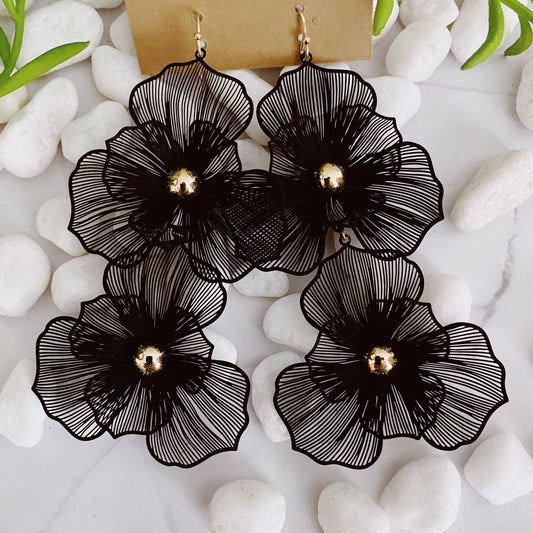 Black floral dangle earrings with golden accents displayed on smooth white stones, creating a stylish and elegant accessory.