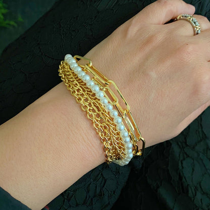 Gold and pearl layered bracelet worn on a woman's wrist, showcasing unique chain links and elegant pearls against a black textured background.