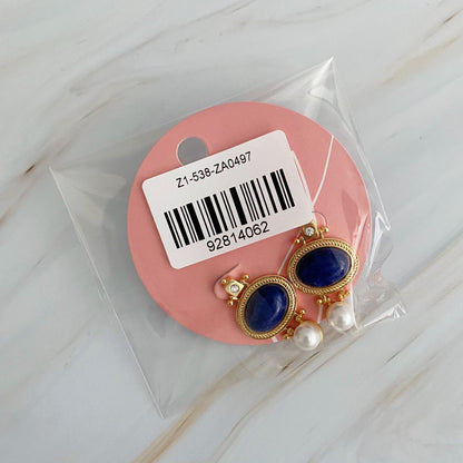 Gold and blue stone earrings with pearl accents in clear packaging on a pink backing