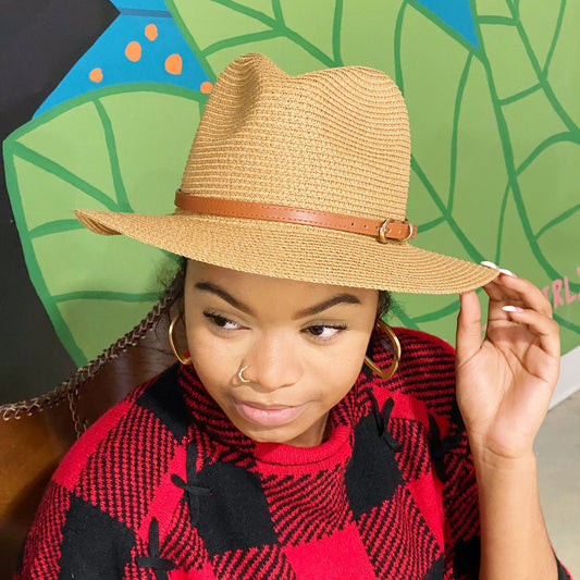 Stylish tan straw hat with brown leather band, perfect for summer fashion, worn by a person in a cozy red checkered sweater against a colorful background.