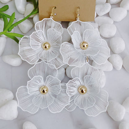 Elegant white floral earrings with gold accents displayed on a neutral background surrounded by smooth white stones.