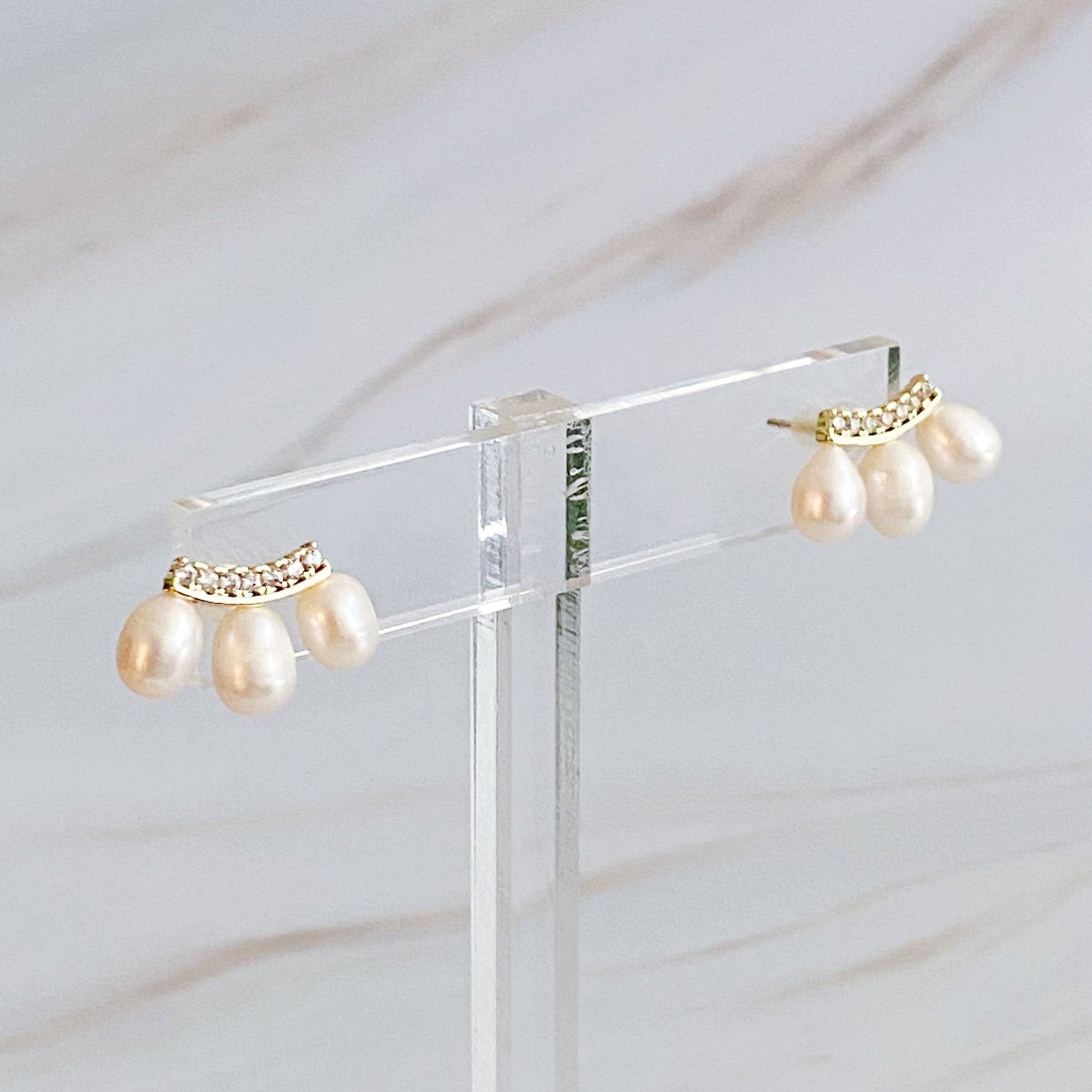 Elegant pearl drop earrings featuring a gold accent with rhinestones, displayed against a light marble background.