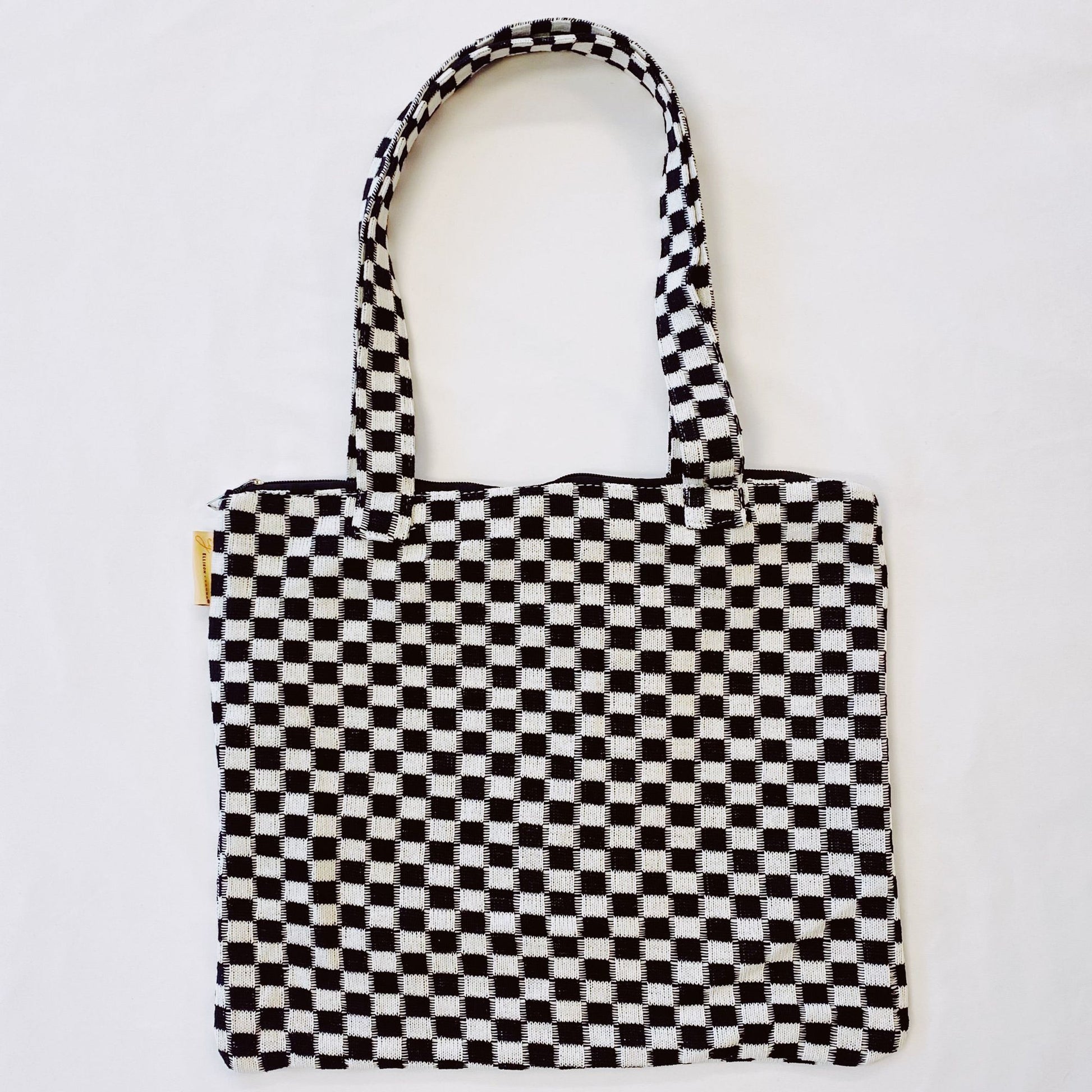 Black and white checkered tote bag with sturdy handles and a zipper closure, perfect for everyday use and stylish shopping.