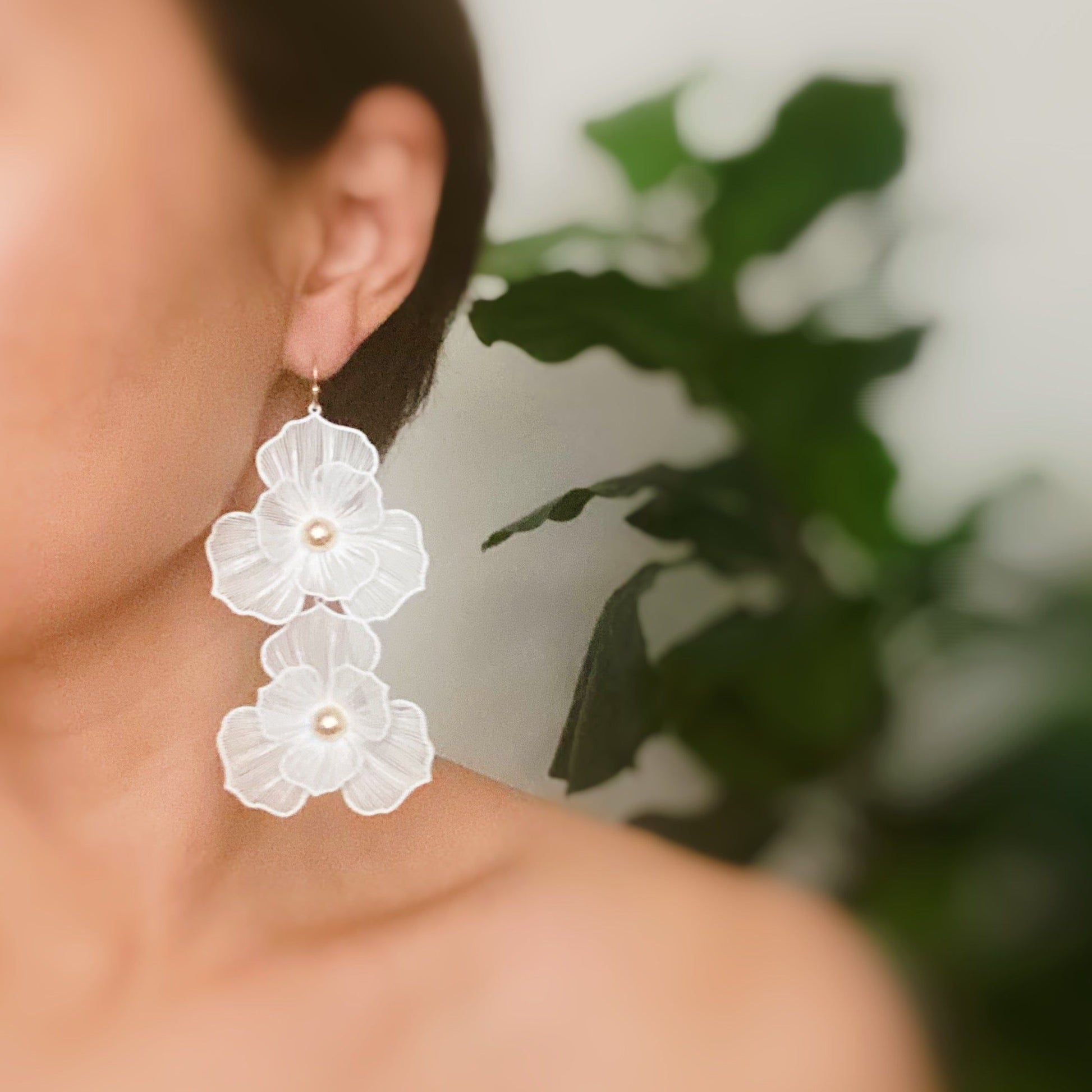 Elegant white flower earrings featuring pearl accents, showcased on a model against a soft green backdrop.